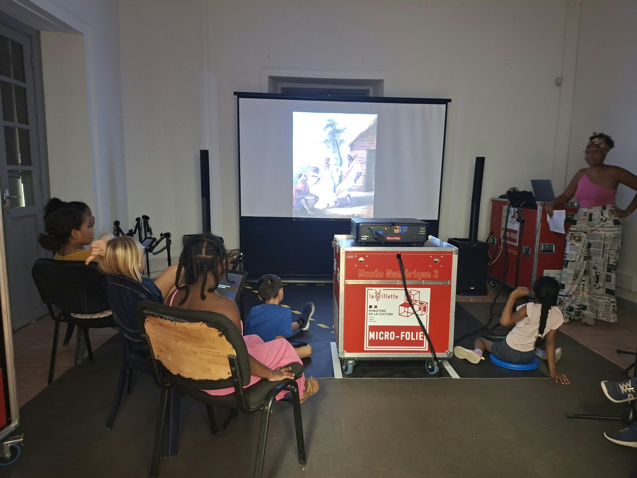 Une médiatrice anime une séance de la Micro-Folie auprès d’enfants assis face à une œuvre projetée.